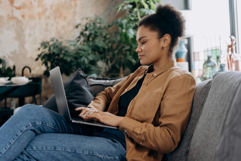 A young woman in casual clothing works on her laptop in a cozy home office setting.