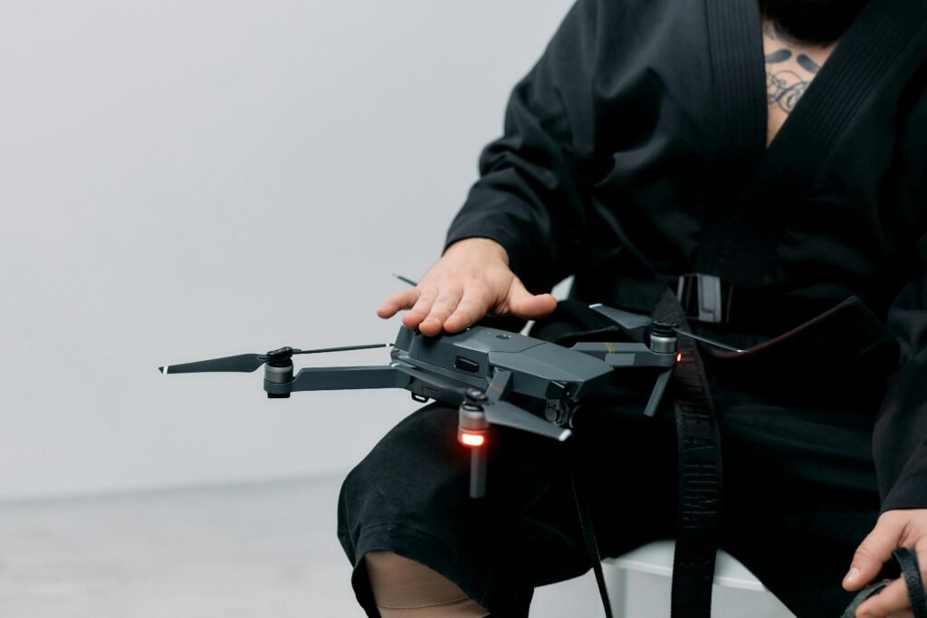 Person in a black robe handling a drone on lap in a studio setting.